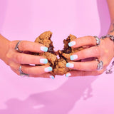 Sticky Toffee Pudding New York Cookie broken in half showing gooey sticky toffee centre held by hands with gradient blue nails